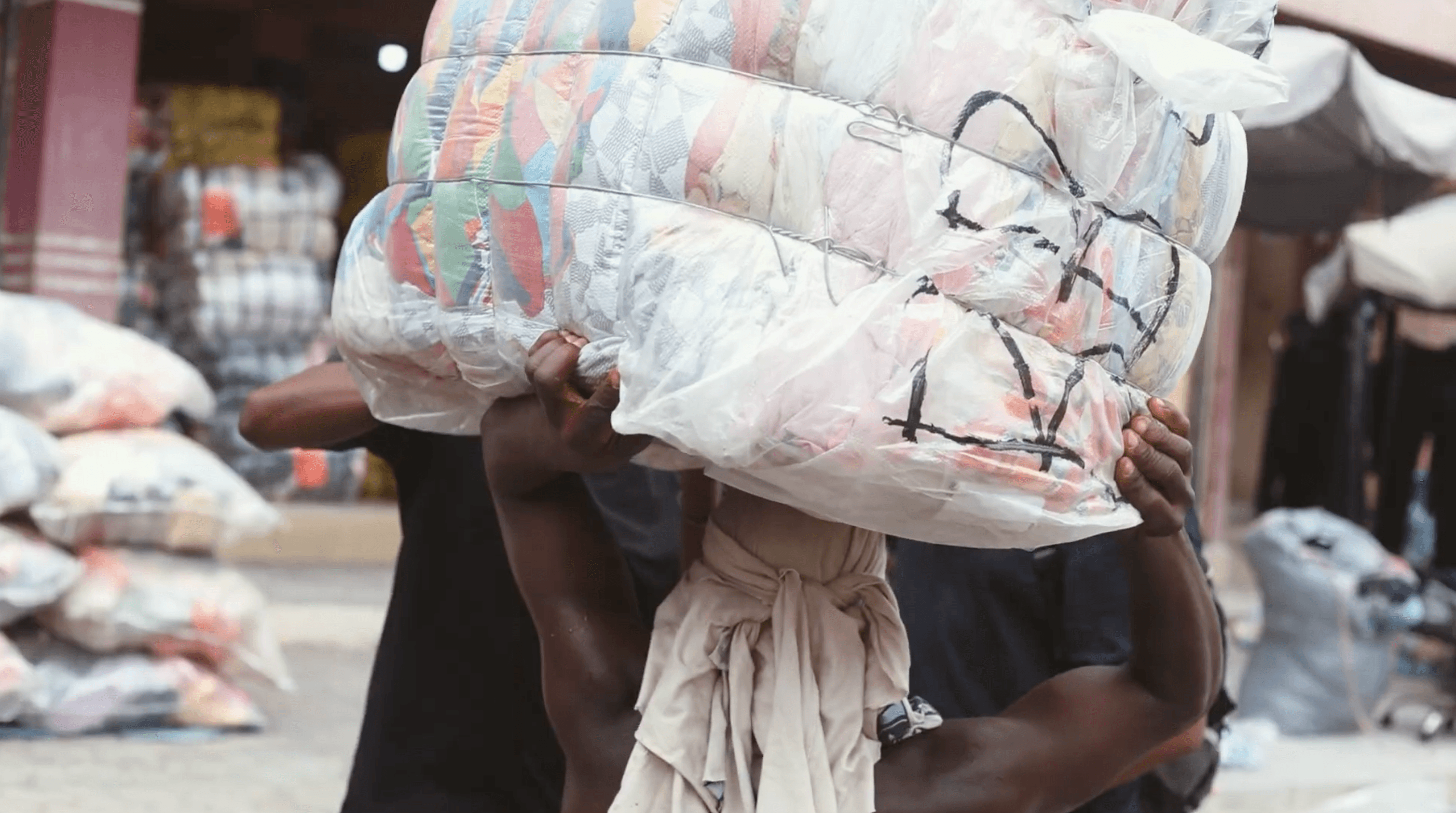 Photo of a person carrying a textile bale in kantamanto market